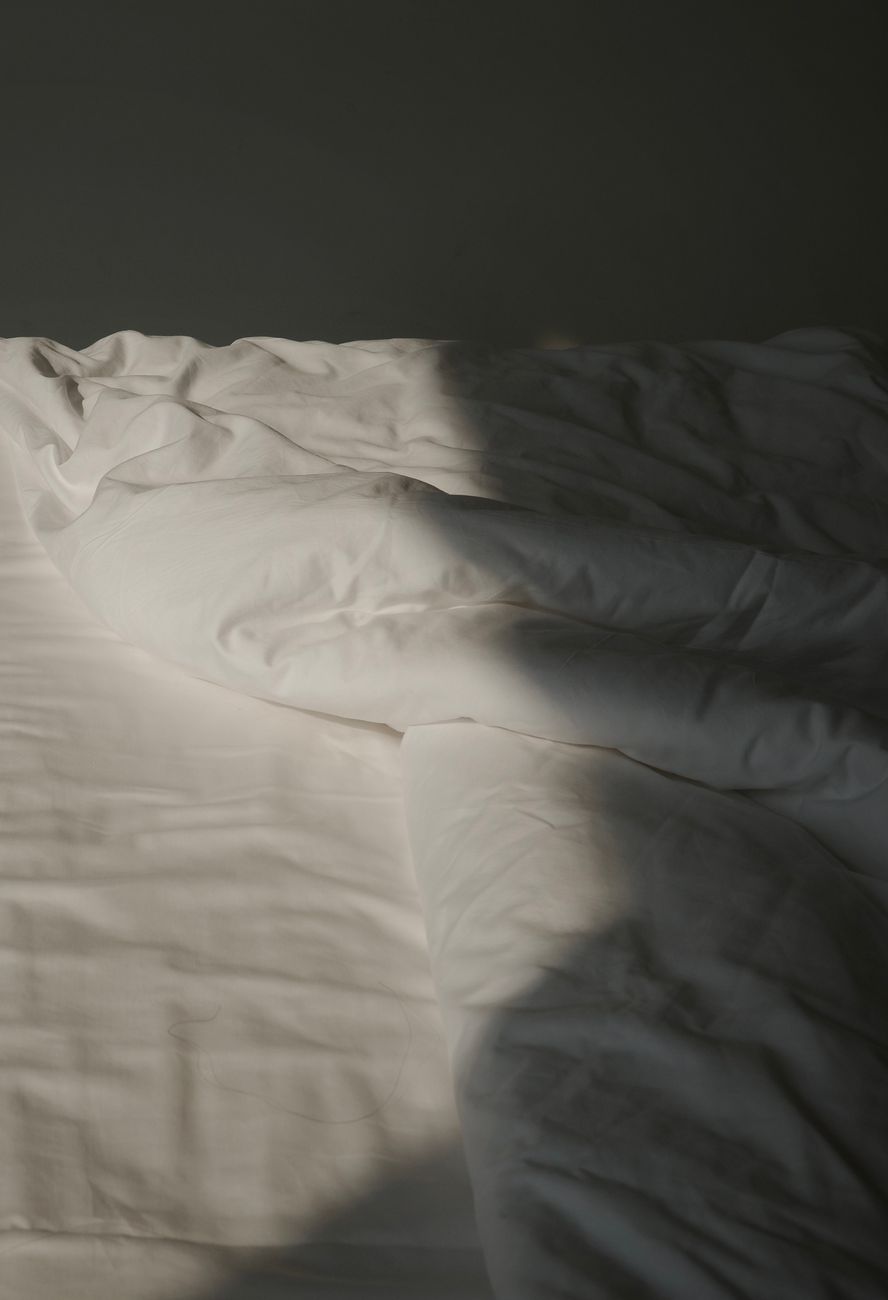 A softly rumpled white bed in raking morning light — the specimen view of heritage bed linen filed by weave, gsm, and years of use.