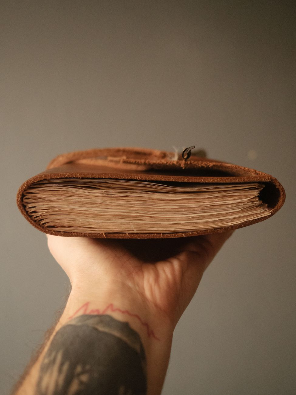 A hand cradling a rustic leather notebook cover with visible stitch and edge burnish — the specimen view of a refillable Cat-1 cover system.
