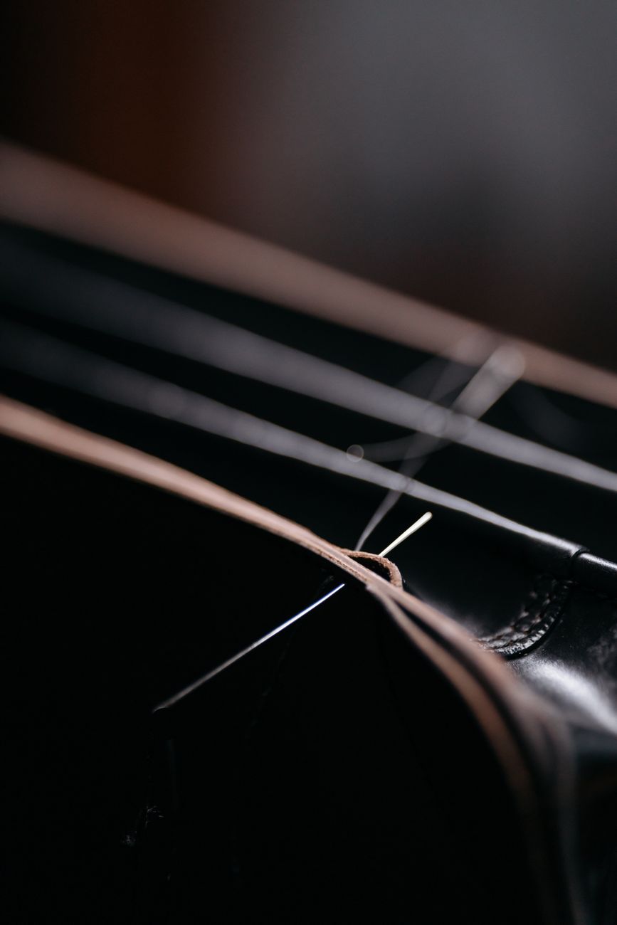 A needle threading through leather in a close macro shot — the hand-stitch stage that separates a maker-signed cover from a machine-run product.