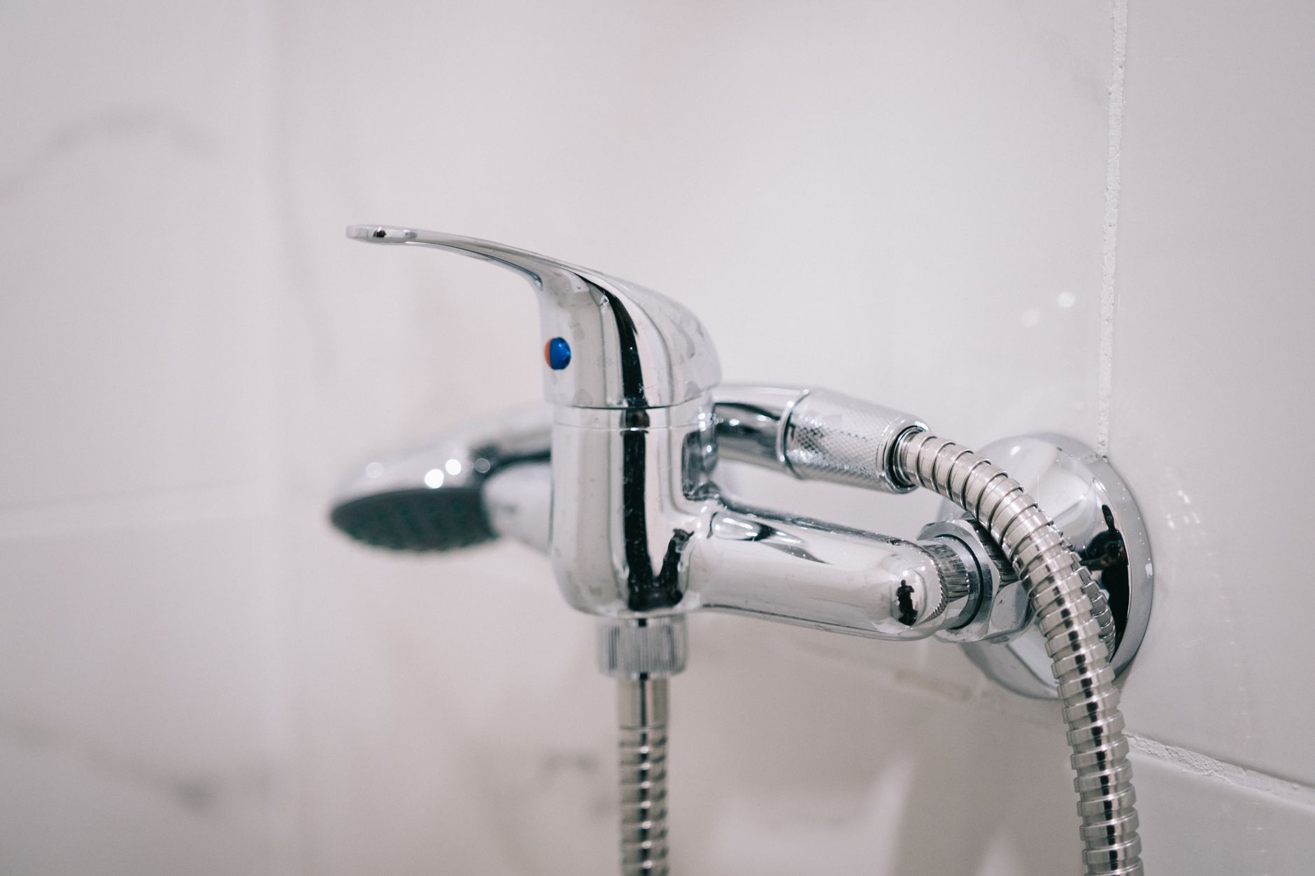 A detailed view of a chrome shower faucet in a clean bathroom — the handheld component of a dual shower head system.
