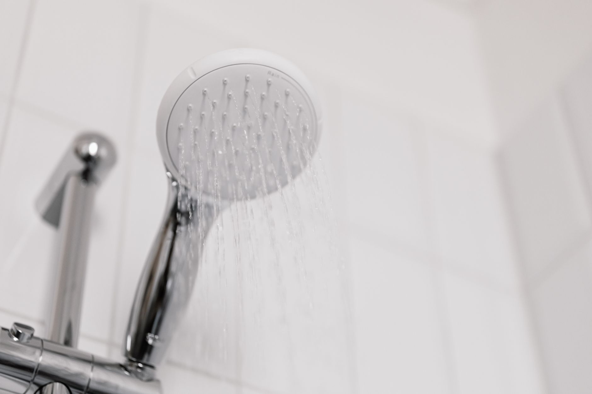 Close view of a clean chrome shower head with water flowing — the macro detail of a rainfall head's spray pattern.