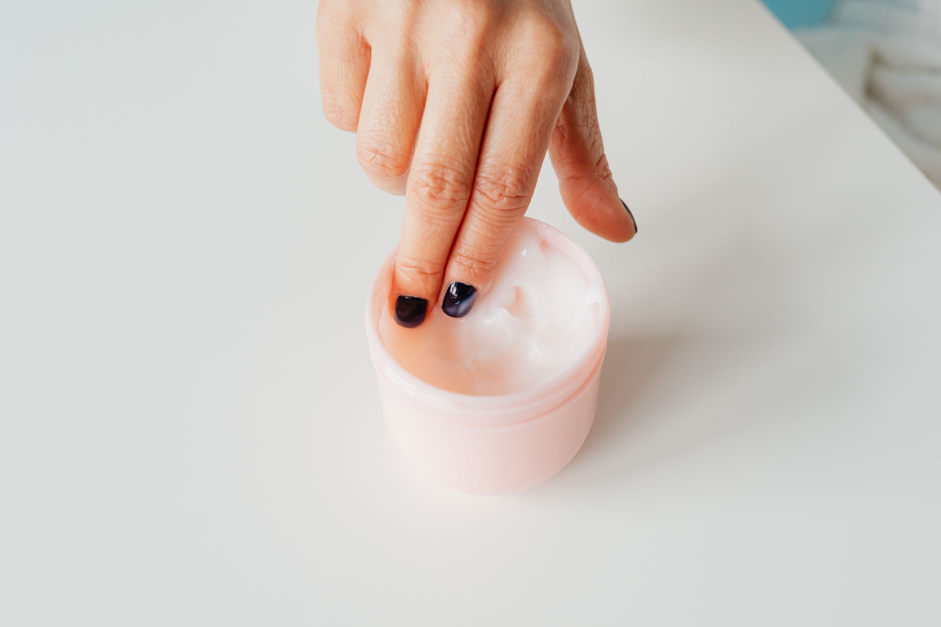 A hand dipping into a white ceramic jar of face cream — the entry point of a French pharmacy skincare routine.